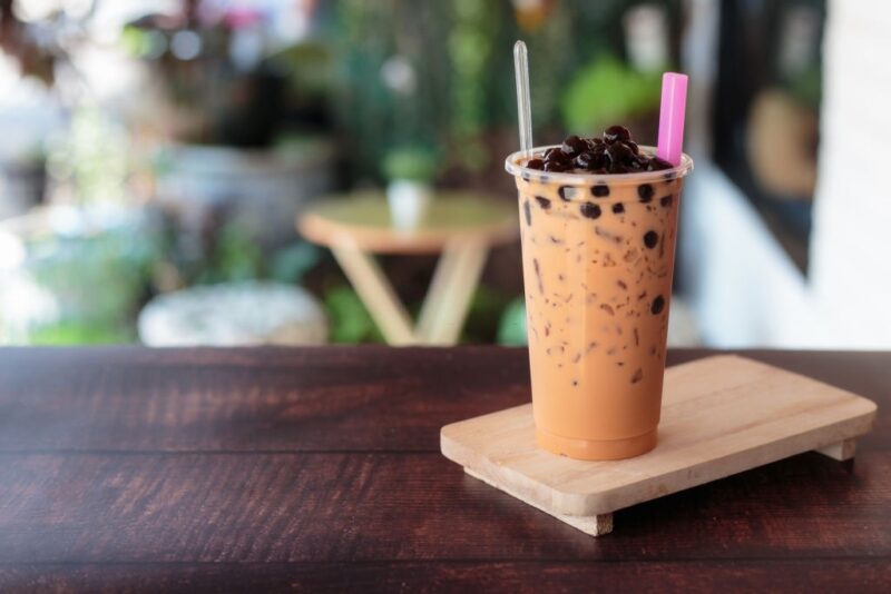 Ice bubble milk tea in takeaway glass on wooden plate - burry background