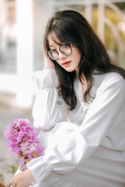 Das Bild eines schönen Mädchens mit langen Haaren, das eine Brille trägt und mit einem Blumenstrauß nachdenkt