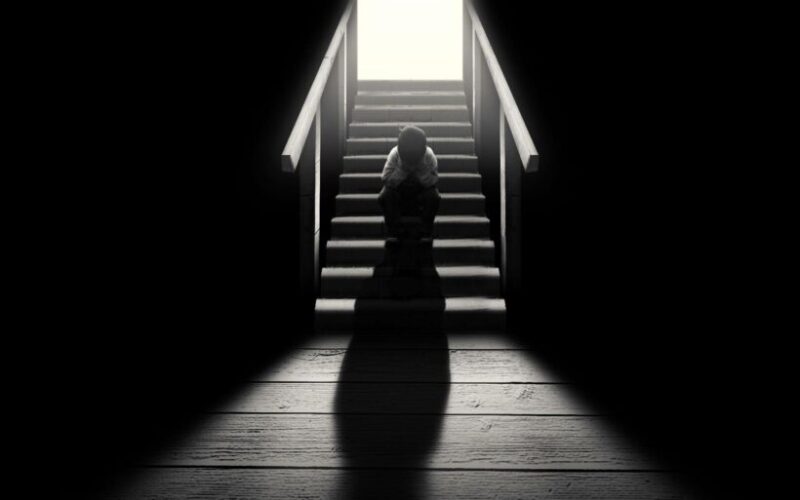 Schwarz-weißes Titelfoto eines Jungen, der allein auf der Treppe sitzt