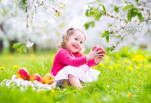 Cô bé vui vẻ ăn táo trong khu vườn nở hoa