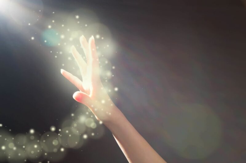 Woman's hand reaching towards glowing light.